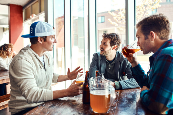 私たちのビールの日付は私たちを正気に保ちます.バーで酒を飲んでいる3人の男性 - 写真・画像