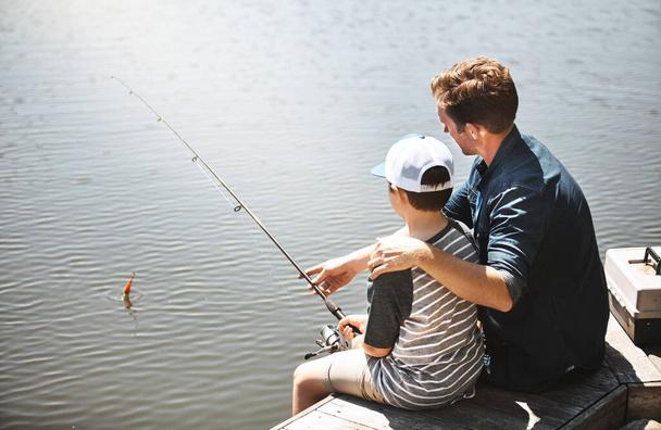 Los papás le enseñan las cuerdas. Vista trasera de un padre y su pequeño hijo pescando juntos - Foto, Imagen