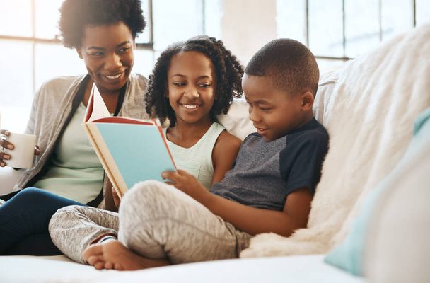 La lectura te enseña a amar de diferentes maneras. un hermano pequeño y una hermana leyendo un libro mientras su madre mira en casa - Foto, Imagen