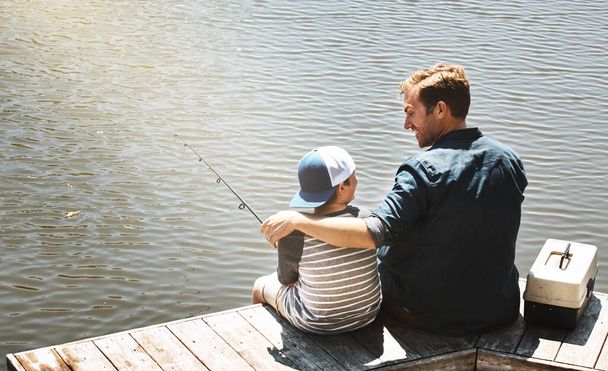 Ze delen dezelfde hobby. Achteraanzicht van een vader en zijn zoontje die samen vissen - Foto, afbeelding