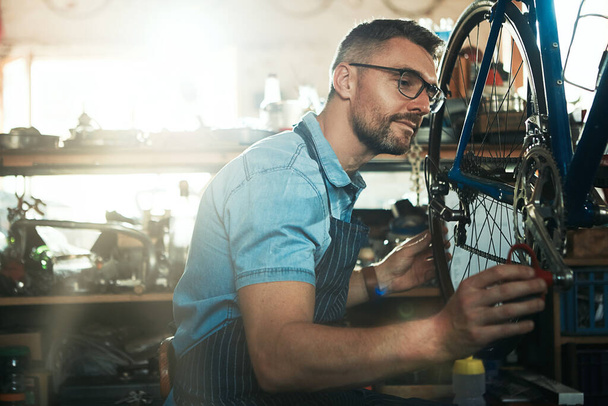 Manos a la obra en el mantenimiento de su bicicleta. un hombre maduro que trabaja en un taller de reparación de bicicletas - Foto, imagen
