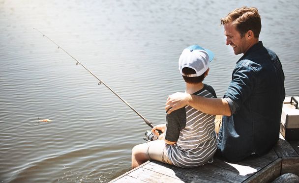 Lo entenderás en poco tiempo. Vista trasera de un padre y su pequeño hijo pescando juntos - Foto, Imagen