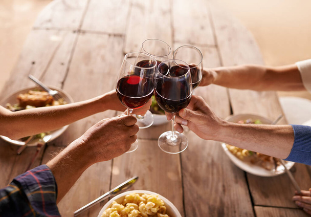 Χέρια, ομάδα και ποτήρι κρασιού για τοστ στο τραπέζι για γιορτή, φαγητό και φίλους στο μεσημεριανό γεύμα. Οι άνθρωποι, μαζί και γιορτάζουν με αλκοόλ, ποτήρια και υποστήριξη στο πάρτι, δείπνο και οικογενειακό σπίτι. - Φωτογραφία, εικόνα