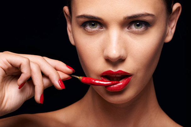 Beauty, portrait and woman with a chilli in a studio for a sensual, glamour and sexy aesthetic. Cosmetic, makeup and female model with a pepper with red lipstick isolated by a dark black background - Фото, зображення