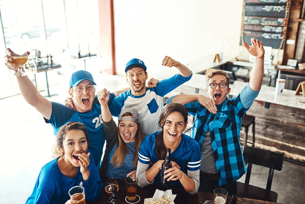 Feliz día de juego Que gane el mejor equipo. un grupo de amigos animando mientras ve un partido de deportes en un bar - Foto, imagen