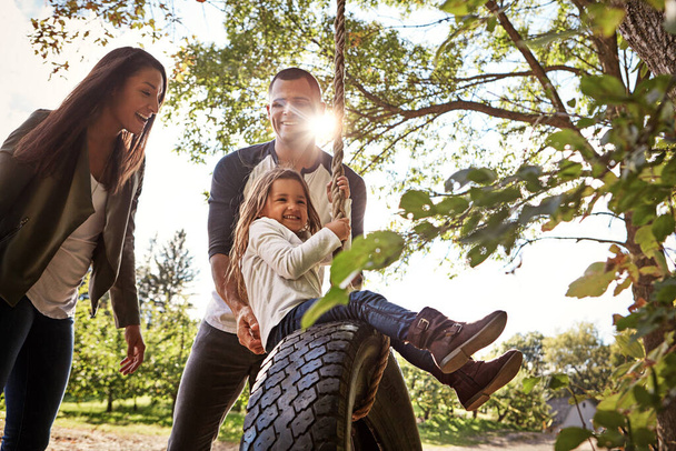 Haciendo tiempo para la gente que más importa. una madre y un padre felices empujando a su hija en un columpio de neumáticos - Foto, imagen