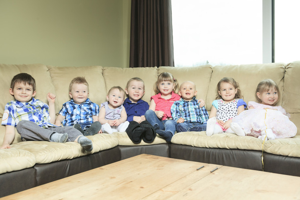 восемь маленьких детей сидят на диване в гостиной
. - Фото, изображение