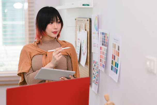 Yaratıcı genç grafik tasarımcısı örnekleyiciden bir renk seçiyor ve iş yerindeki dijital tablet bilgisayarda çiziyor - Fotoğraf, Görsel