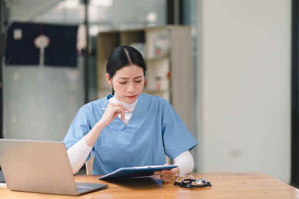 Концентрированная женщина-врач или медсестра работает онлайн с ноутбуком, сидя за столом в больничной консультационной комнате. медицина, технологии и здравоохранение. - Фото, изображение