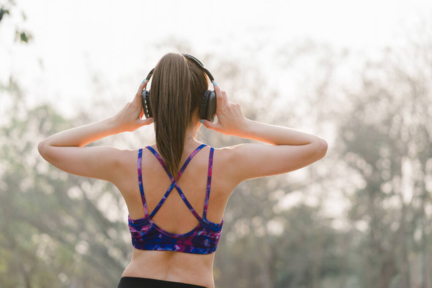 A relaxed woman is shown enjoying music while jogging through a public park. The young lady is feeling free, relaxed, and happy - Фото, изображение