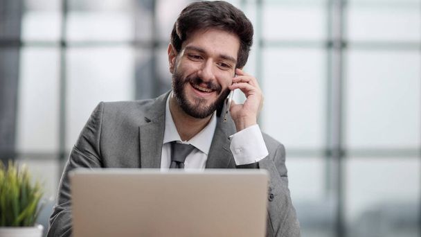 Smiling man while making phone call and using laptop in the office - Foto, Imagen