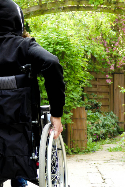 Una persona discapacitada en silla de ruedas. Un hombre con movilidad reducida en un callejón con vegetación. - Foto, imagen