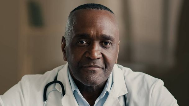 顔の医療ポートレートを閉じます高齢者の男性医師の専門家一般開業医病院での医師の仕事アフリカ民族の男性歯科医医療臨床セラピストカメラの健康管理の概念を見て - 写真・画像