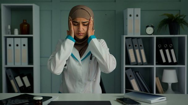Chory arabski muzułmanin kobieta przeciążony zmęczony pracownik medyczny lekarz lekarz cierpi na ból głowy dotyk głowy pocierać skronie uczucie niezbyt dobrze ból przewlekła choroba migrenowa zdrowie choroby z powodu przepracowania w szpitalu - Zdjęcie, obraz