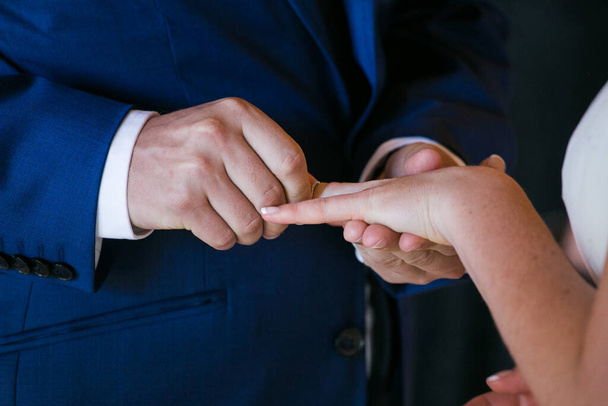 This beautiful image captures the intimate moment of a couple exchanging wedding rings at a real wedding. The photograph features a close-up of the couple's hands, showcasing their intertwined fingers and the wedding bands on their fingers. The image - Fotografie, Obrázek