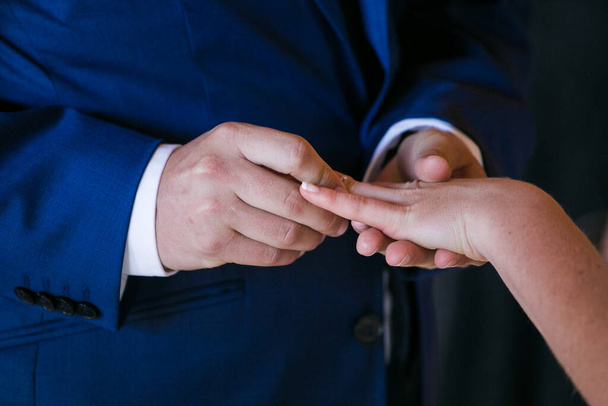 This beautiful image captures the intimate moment of a couple exchanging wedding rings at a real wedding. The photograph features a close-up of the couple's hands, showcasing their intertwined fingers and the wedding bands on their fingers. The image - Фото, зображення