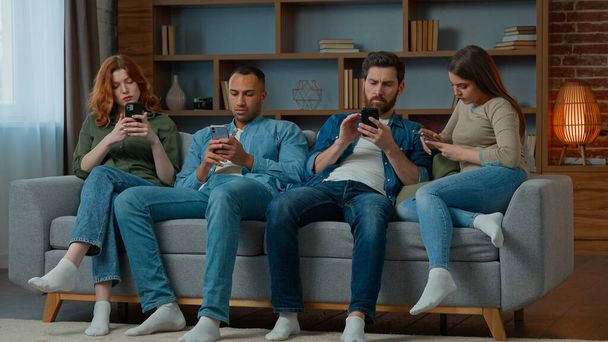 Grupa przyjaciół biznesowych ludzie siedzą na kanapie z telefonami komórkowymi na czacie w mediach społecznościowych ignorując się nawzajem wielonarodowe uzależnione kobiety i mężczyźni używają różnych urządzeń nowoczesne gadżety uzależnienia tech overuse - Zdjęcie, obraz