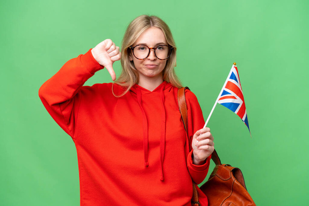 Junge hispanische Frau mit einer britischen Flagge vor isoliertem Hintergrund, die den Daumen mit negativem Ausdruck nach unten zeigt - Foto, Bild