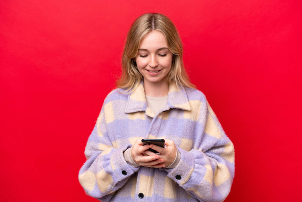 Jeune Anglaise isolée sur fond rouge envoyant un message avec le mobile - Photo, image