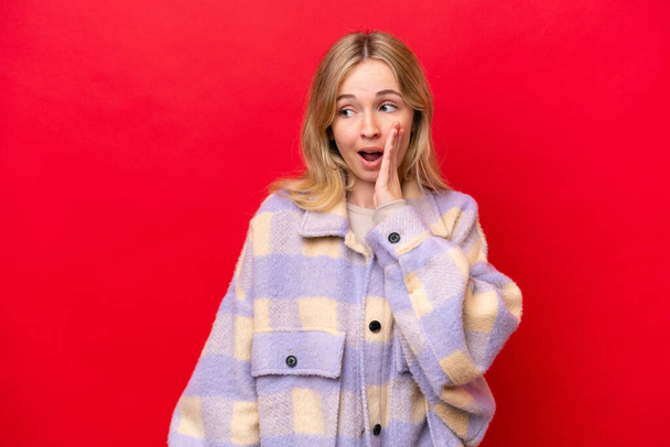 Young English woman isolated on red background whispering something with surprise gesture while looking to the side - Foto, immagini
