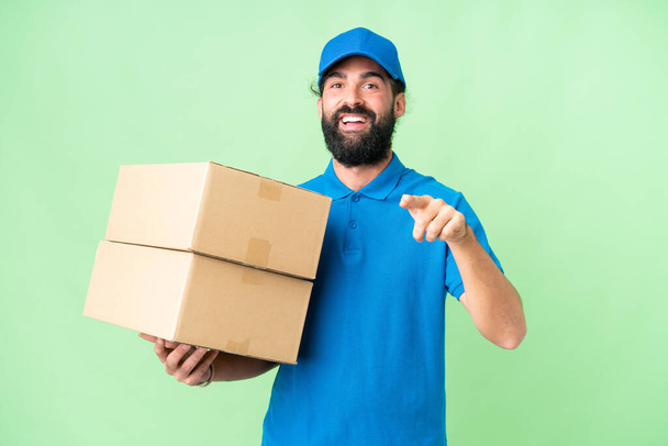 Delivery caucasian man over isolated chroma key background surprised and pointing front - Foto, imagen