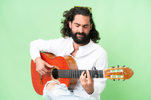 Young man with beard with guitar over isolated chroma key background - 写真・画像