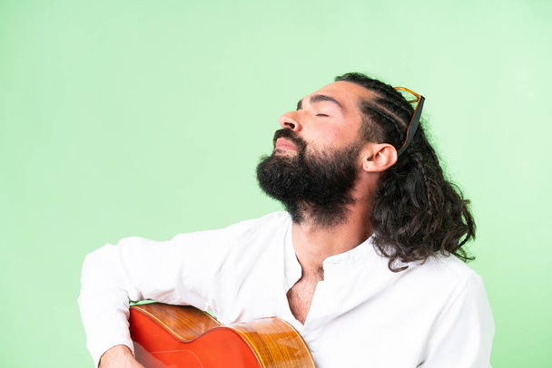 Молодой человек с бородой и гитарой на изолированном фоне хромы - Фото, изображение