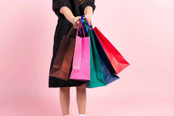 Shopping per bambini. irriconoscibile bambina in nero elegante abito estivo in posa con borse della spesa. Isolato su sfondo rosa. - Foto, immagini