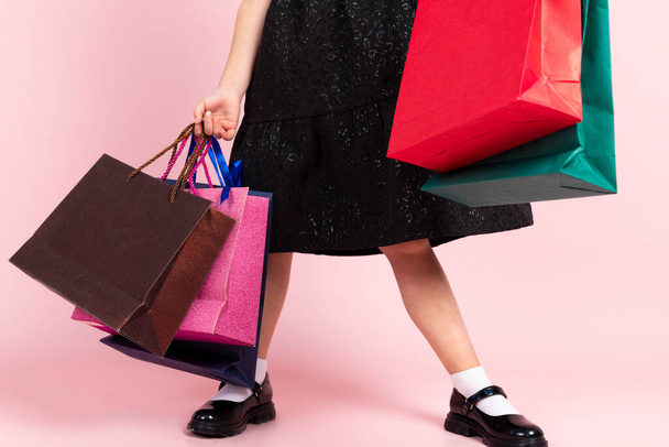 Nakupování dětí. nepoznatelná holčička v černých stylových letních šatech pózuje s nákupními taškami. Izolované na růžovém pozadí. - Fotografie, Obrázek