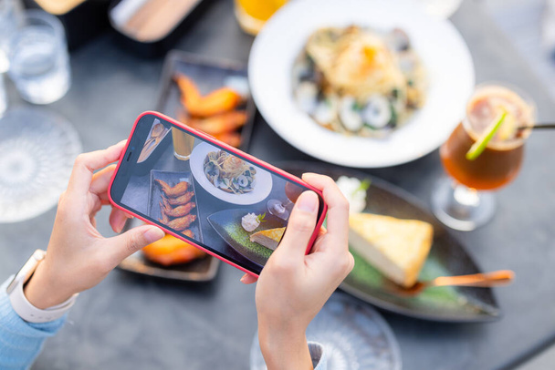 Жінка використовує мобільний телефон, щоб сфотографуватися в ресторані
 - Фото, зображення