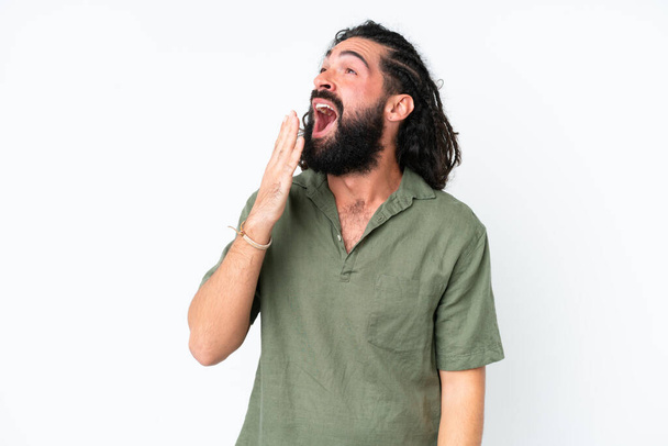 Νεαρός άνδρας με γενειάδα πάνω από απομονωμένο λευκό φόντο χασμουριέται και καλύπτει το ανοιχτό στόμα με το χέρι - Φωτογραφία, εικόνα