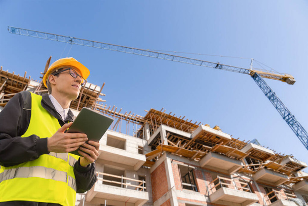 Engineer with a digital tablet on the background of a building under construction. High quality photo - Foto, Imagen