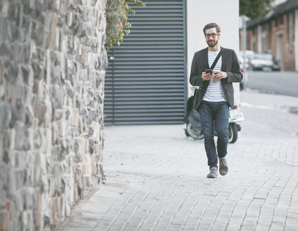 Te voet de stad verkennen. een stijlvolle jongeman met een mobiele telefoon in de stad - Foto, afbeelding