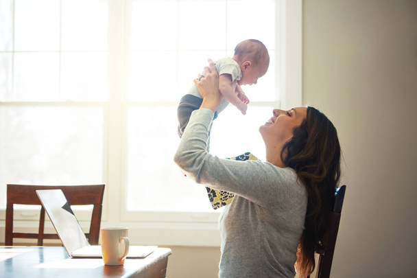 Насолоджуйся цим моментом. мати тримає свою новонароджену дитину, сидячи за столом перед ноутбуком
 - Фото, зображення