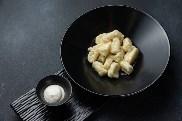 A bowl of gnocchi with a side of sour cream. - Zdjęcie, obraz
