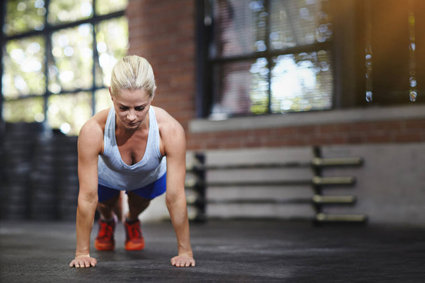 Her body is a precision instrument. a young woman doing pushups in a gym - Foto, Imagem