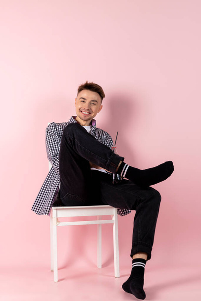 Un joven feliz sentado con una botella de coca. comida rápida y adicción al azúcar. Aislado sobre fondo rosa. - Foto, Imagen