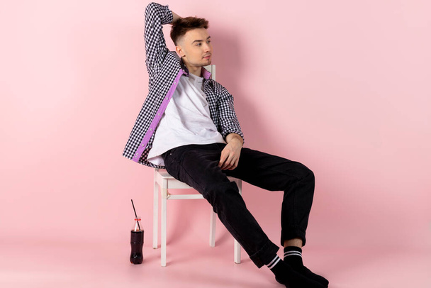 A happy young man sitting with a bottle of coke. fast food and sugar addiction. Isolated on pink background. - Foto, Imagen