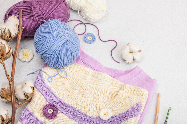Ręcznie szydełkowana koszulka niemowlęca w kolorze liliowym. Rzeczy i rekwizyty zawiera nici, haki, druty i rzemieślnicze wystrój. Jasny kamień beton tło, widok z góry - Zdjęcie, obraz