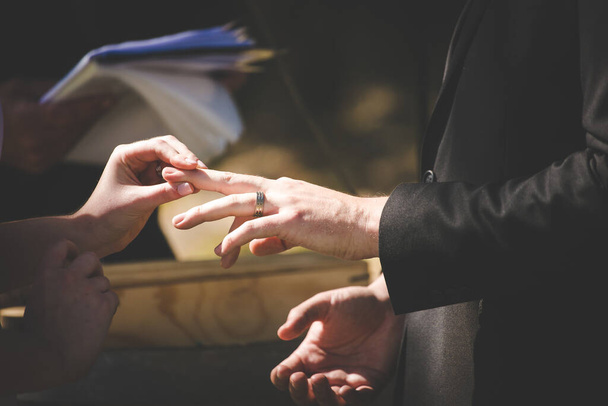 This beautiful image captures the intimate moment of a couple exchanging wedding rings at a real wedding. The photograph features a close-up of the couple's hands, showcasing their intertwined fingers and the wedding bands on their fingers. The image - Valokuva, kuva
