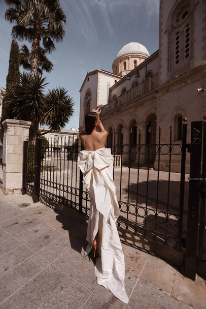 модная открытая фотография красивой женщины с темными волосами в роскошном свадебном платье с аксессуарами, позирующими на улице античного города - Фото, изображение
