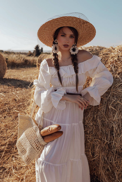 fashion outdoor photo of beautiful woman with dark hair in elegant white dress with accessories posing in hayloft - 写真・画像