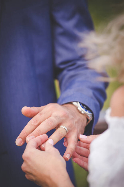 This beautiful image captures the intimate moment of a couple exchanging wedding rings at a real wedding. The photograph features a close-up of the couple's hands, showcasing their intertwined fingers and the wedding bands on their fingers. The image - 写真・画像