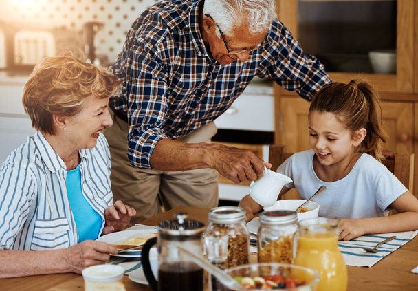 Laat opa je daarmee helpen, lieverd. een klein meisje ontbijten met haar grootouders thuis - Foto, afbeelding
