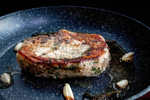 Grilled premium rib eye beef steak in the pan, cooking steak in the kitchen on a dark background. Overhead shot of chef preparing ribeye with butter, thyme and garlic - Foto, imagen