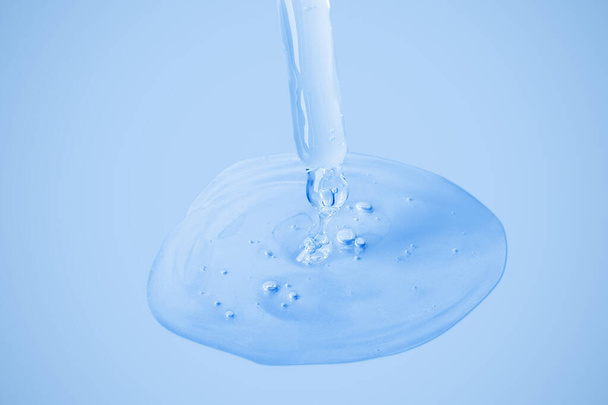 Transparent cosmetic gel flows from an eyedropper directly onto the background in a large blob with bubbles. On a blue background. Hyaluronic acid, toner, toner, gel, cream. Cosmetics. - Photo, Image