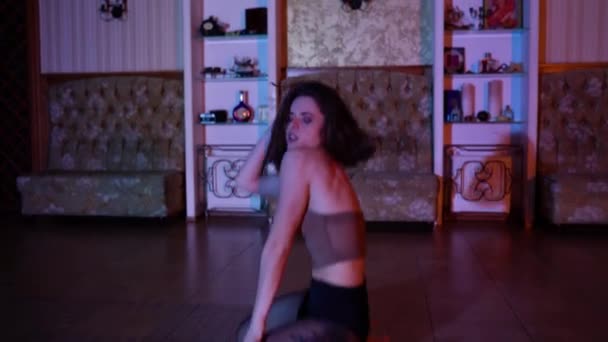 Сексуальная брюнетка на высоких каблуках танцует на полу в красочной освещенной комнате. Высококачественные 4k кадры - Кадры, видео