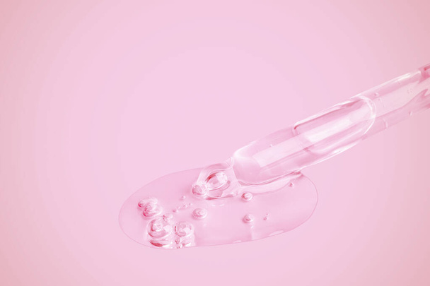 Un gel trasparente che scorre da una pipetta. Un sacco di gel fluente in una grande goccia. Con le bolle. Su uno sfondo rosa. - Foto, immagini