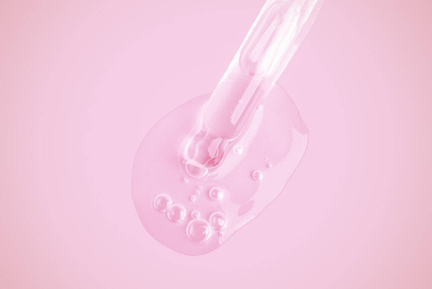 Een vloeiende heldere gel uit een pipet. Veel stromende gel in een grote druppel. Met bubbels. Op een roze achtergrond. - Foto, afbeelding
