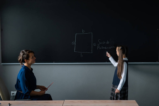 Caucasian little girl answers the question of the female teacher at the blackboard - Φωτογραφία, εικόνα